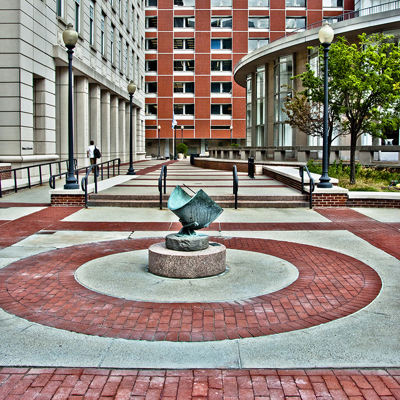 A brick and concrete plaza featuring a small art sculpture at its center