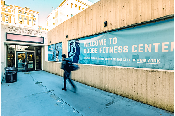 The entrance to the Dodge Fitness Center at Columbia - a student hurries to the entrance with his backpack on his back.