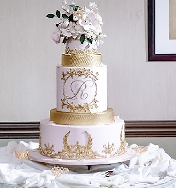 A beautiful pink, three-tier wedding cake, with gold accents and flowers on top.