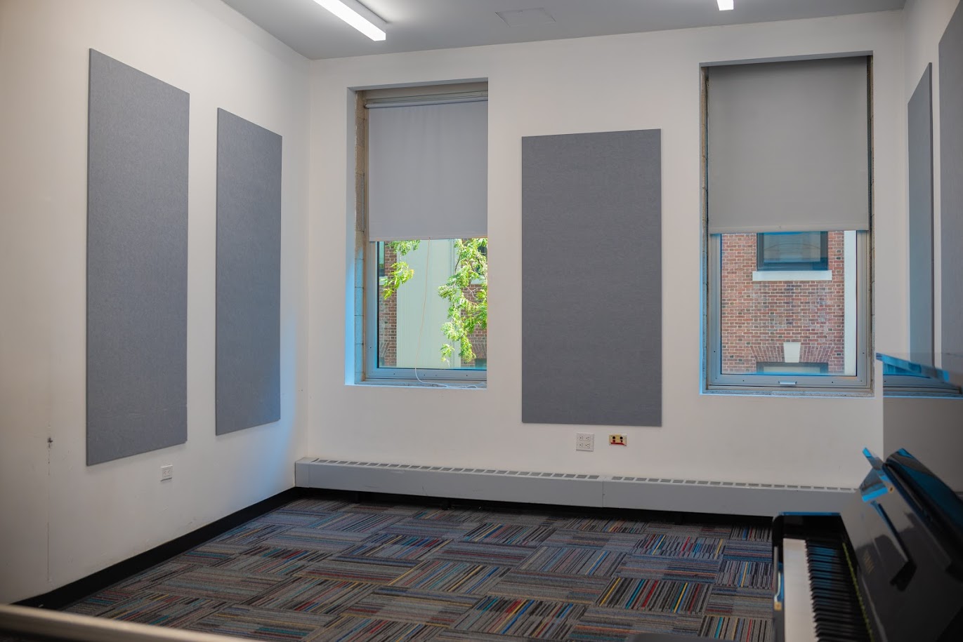 Grey acoustic panels line a white-walled room. A black piano is pushed against one wall.