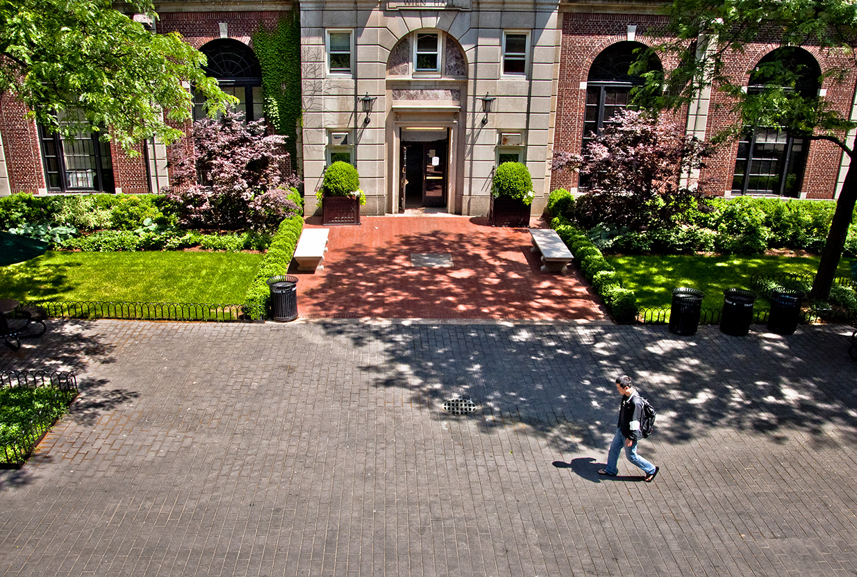 A grey stone paved plaza is in front a brick building. 