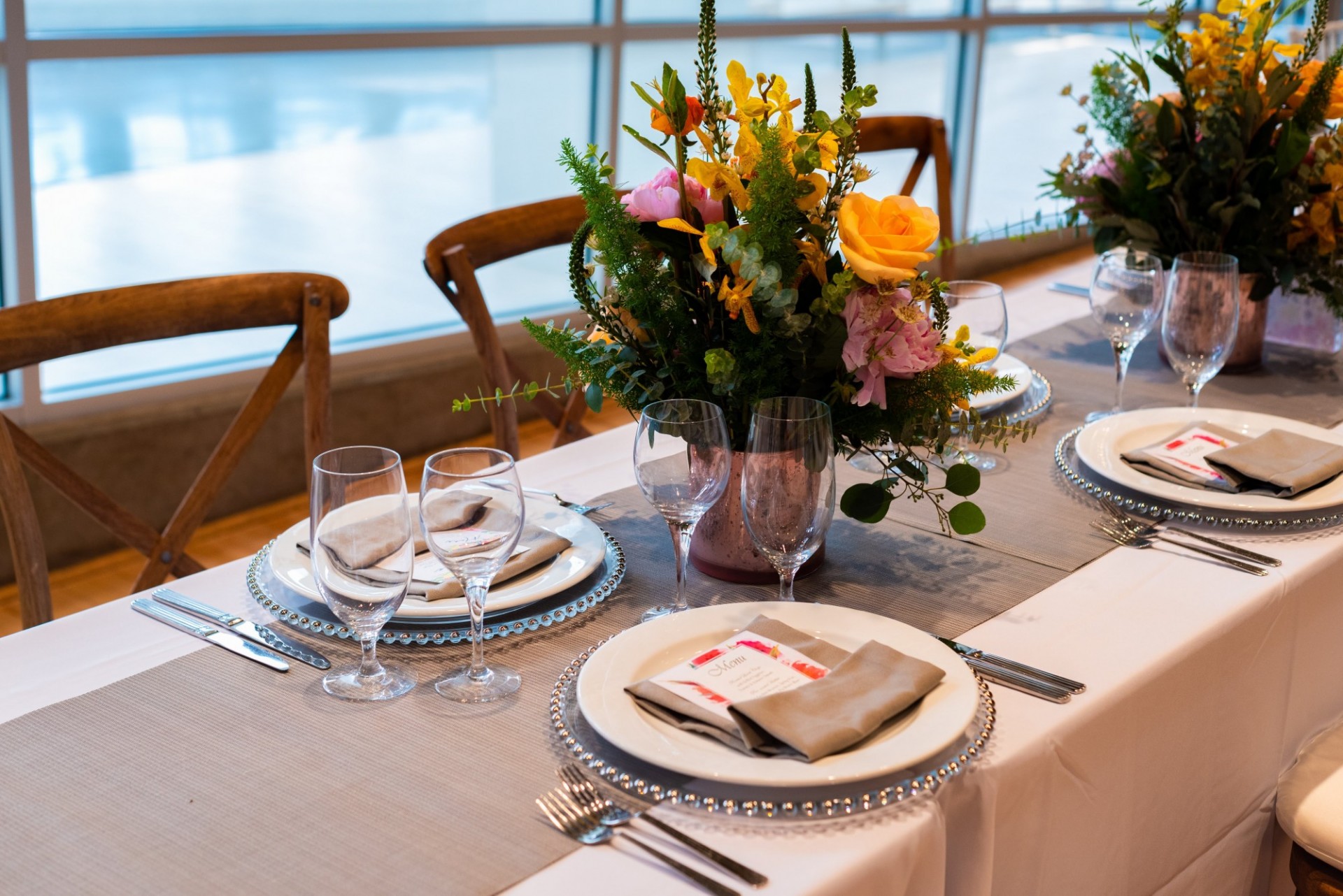 A burlap table runner dresses a long table featuring place settings and flowers in a vase