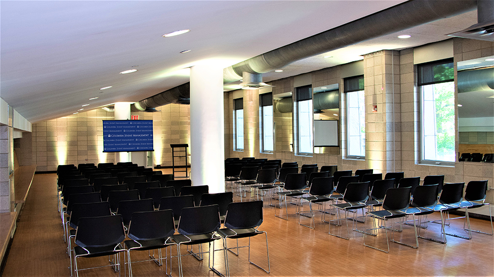 Rows of black chairs face a projector screen and podium. 