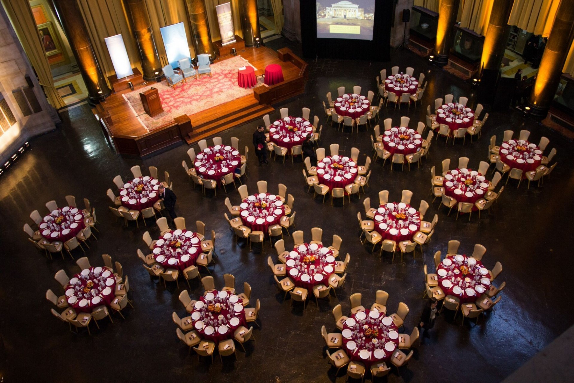 Banquet-style setup with round tables Aerial view of the Rotunda, showing round tables set with red linens and a wooden stage with three chairs.