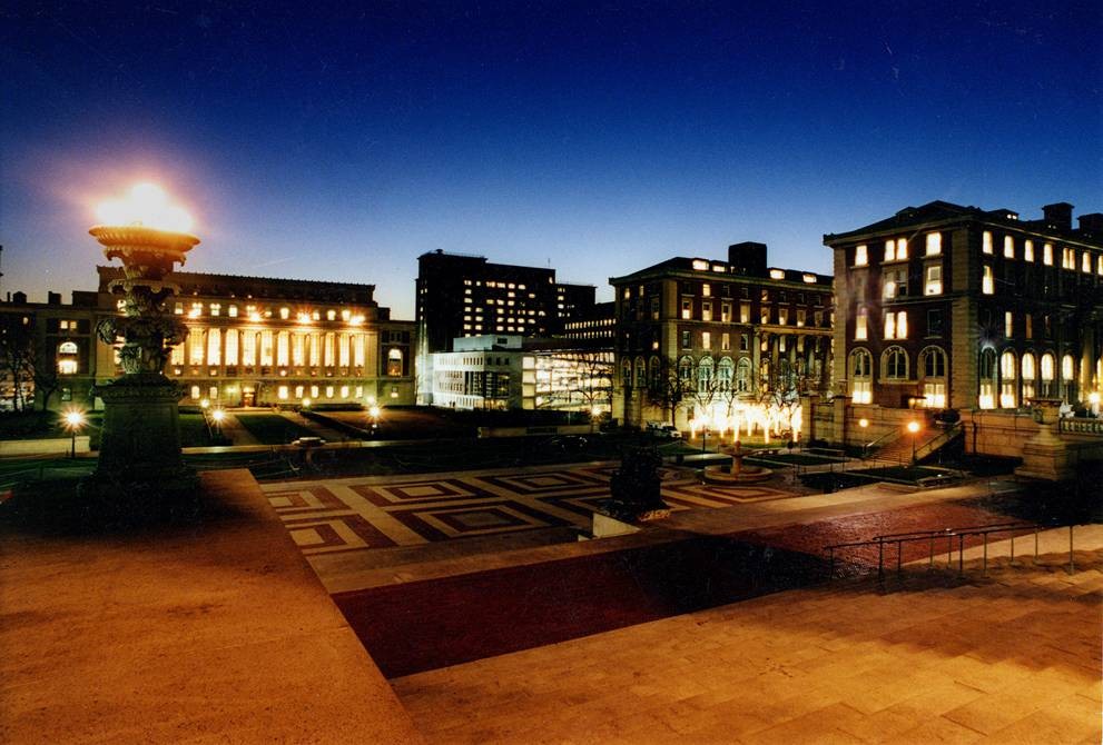 A southern-looking view of Low Plaza taken from the top of Alma Mater steps at dusk. In the background, the columns of Butler Library are illuminated. 
