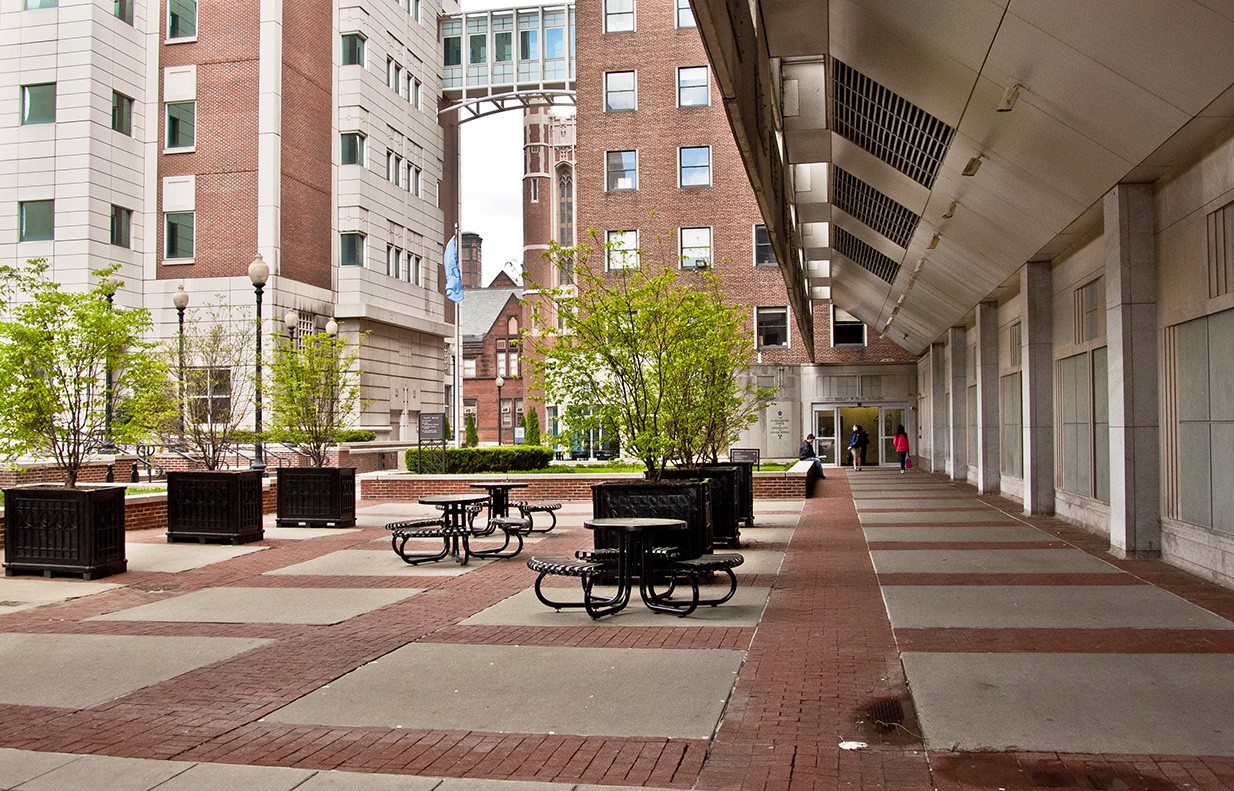 Alternate view of Mudd Terrace: a brick and concrete paved area adjacent to a building overhang. Metal picnic tables dot the area.
