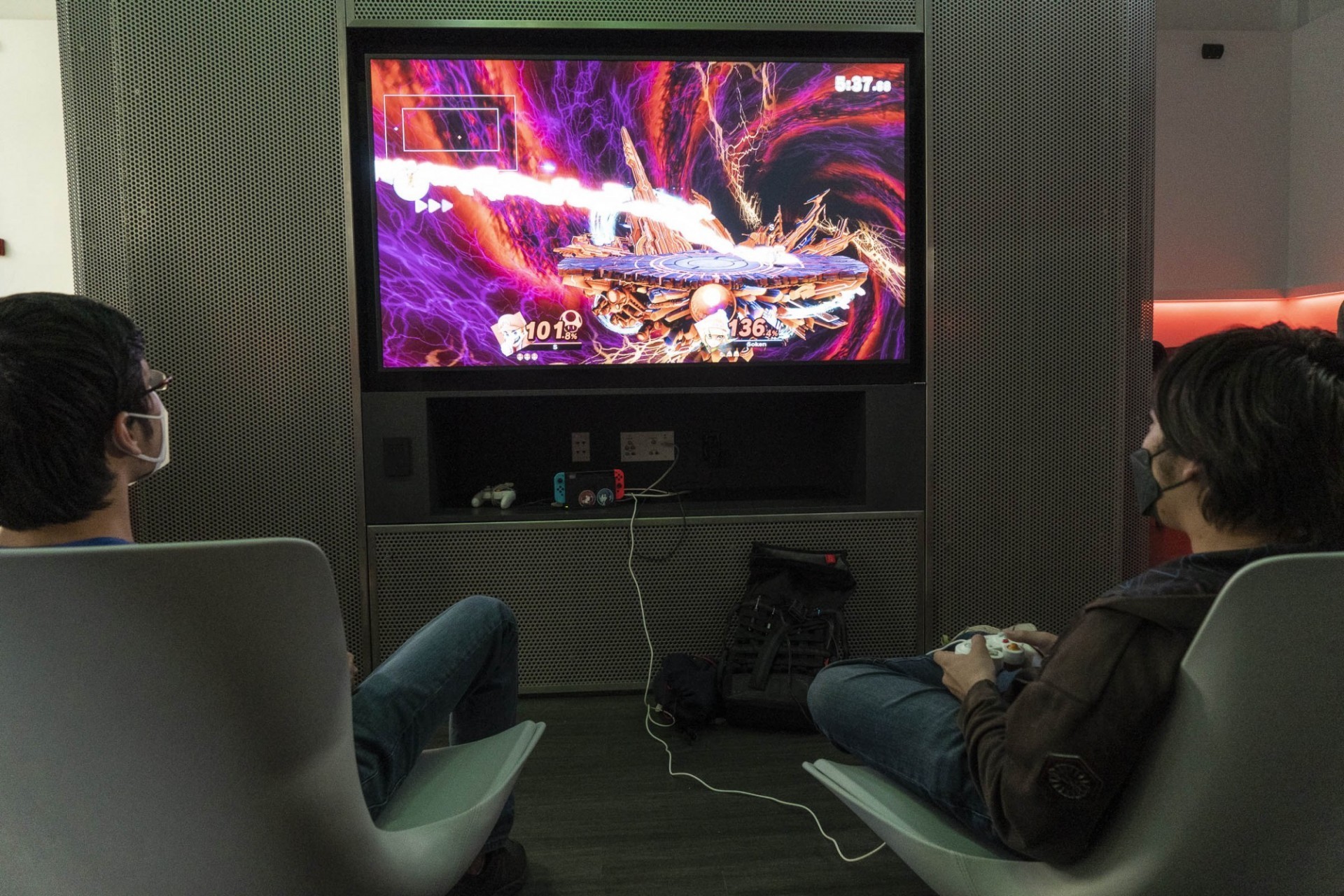 Students sit in high-backed chairs in front of a large screen playing video games in the ESPORTS room
