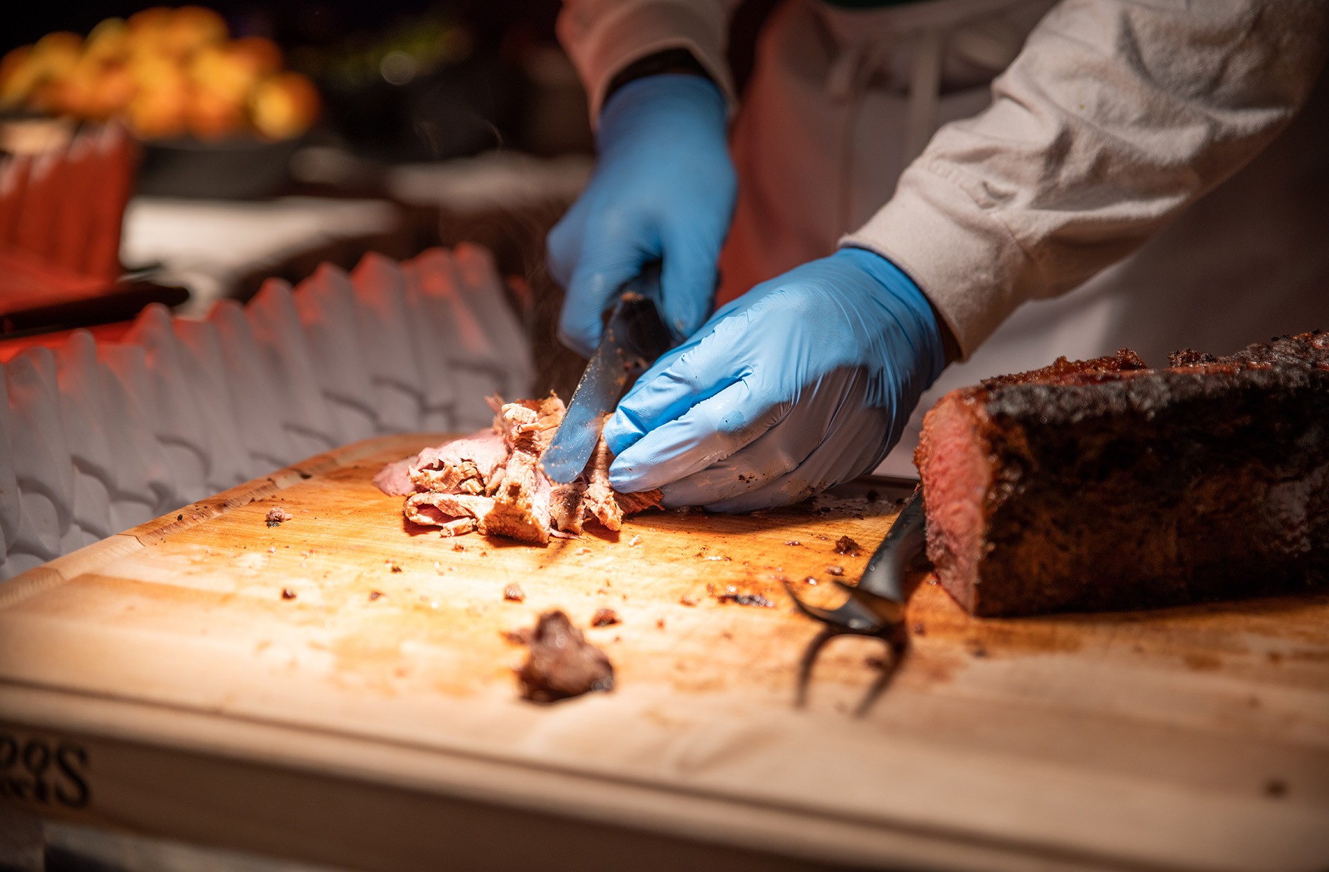 Close up photo of a chef, wearing gloves and carving roast pork to serve to event guests.