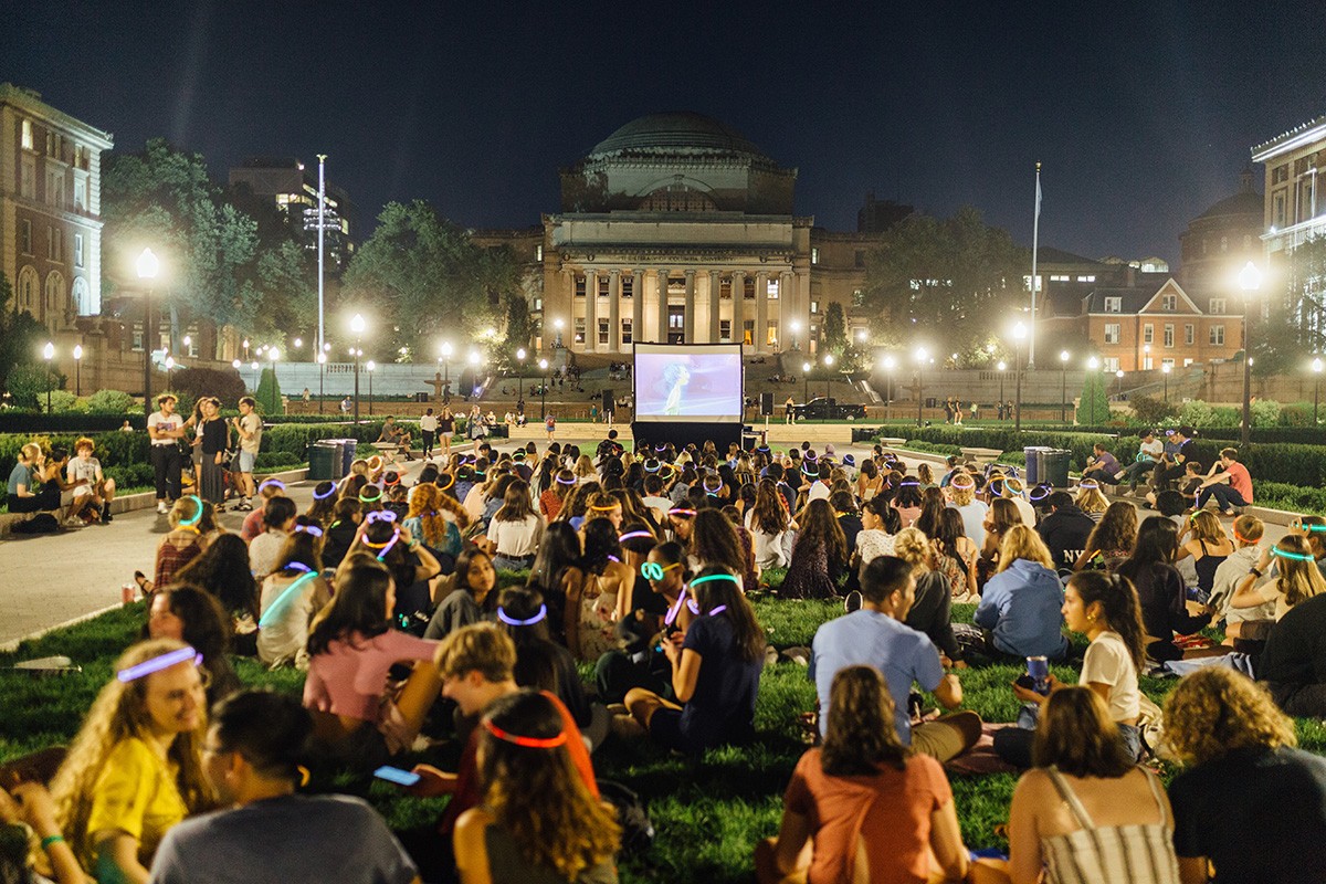 students sit on south lawn watching a movie on a pop-up screen
