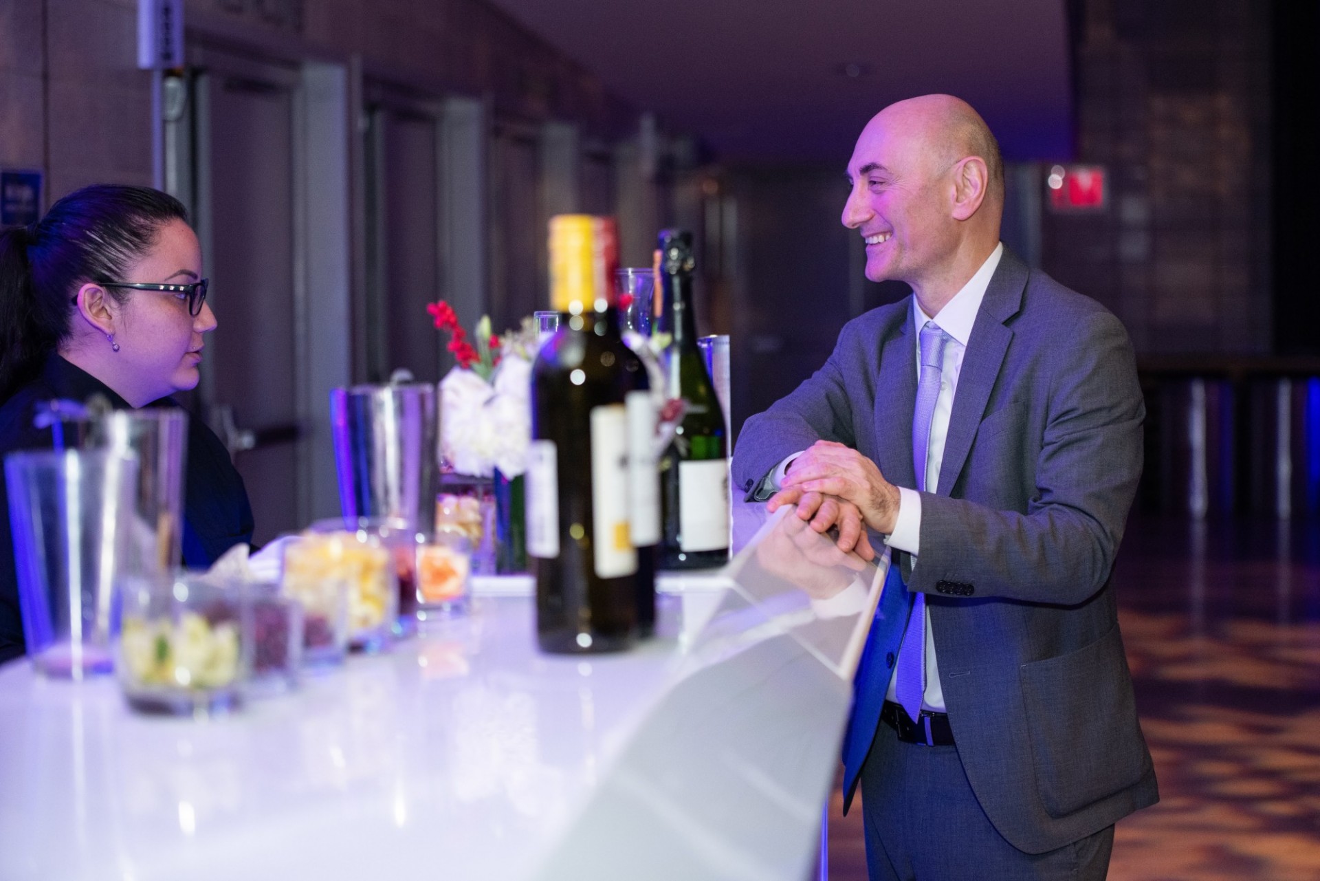 A staff member at an event is getting a drink from the bar, smiling at the bartender.