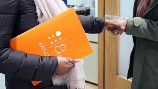 A photo of two people shaking hands, one of whom is holding a folder from Columbia Disability Services.