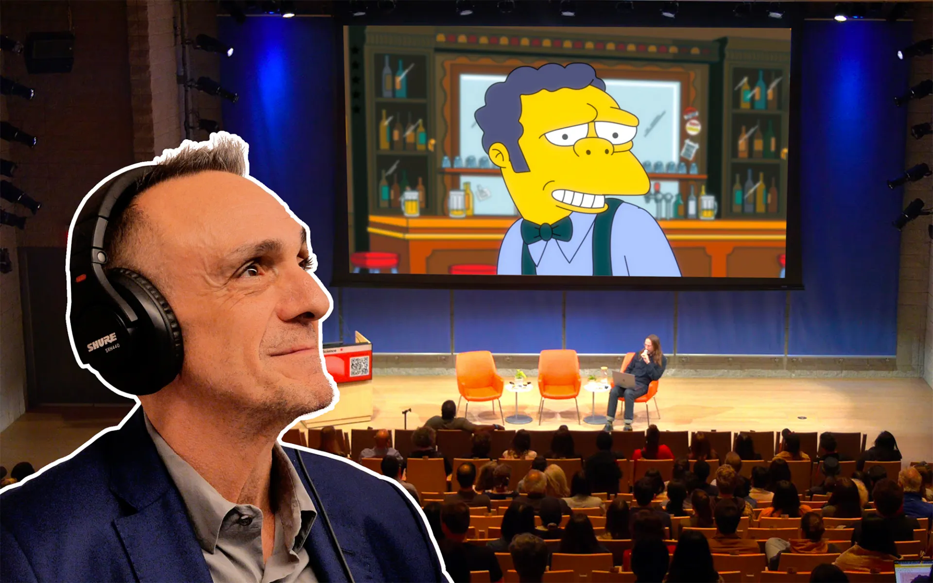 An edit of Hank Azaria over the top of an image of the stage at the Lee C. Bollinger Forum during an event. An image of Moe the Bartender is up on a screen behind the stage.