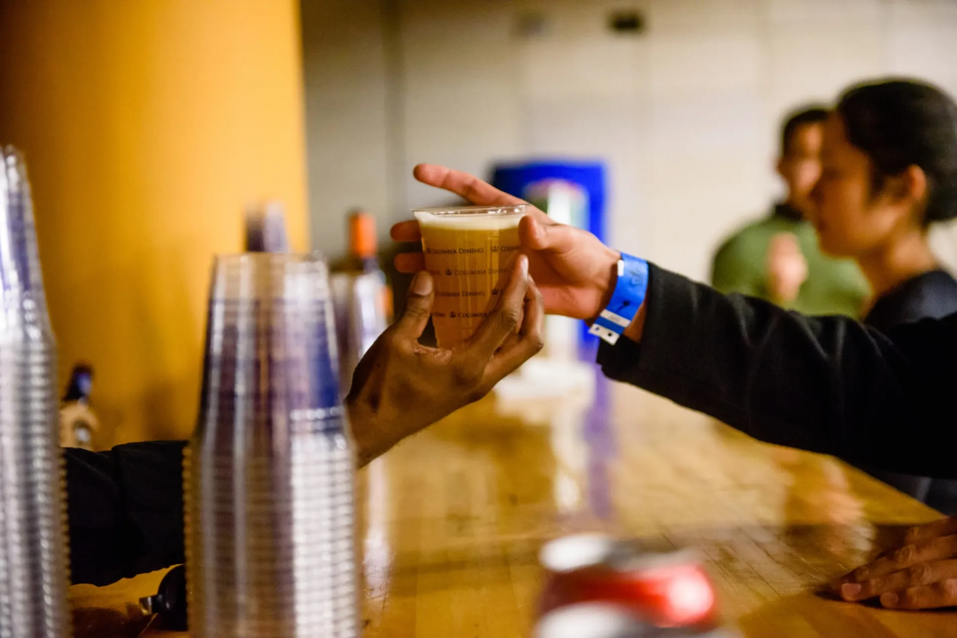 Student wearing a wrist band holds a beer