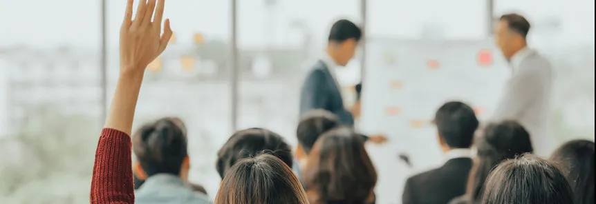 Students in a classroom raising their hands to ask a question of the instructor.