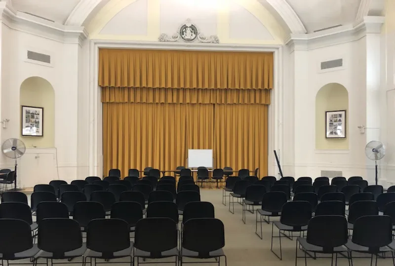 A room in Earl Hall set up with rows of chairs facing a stage with gold curtains drawn