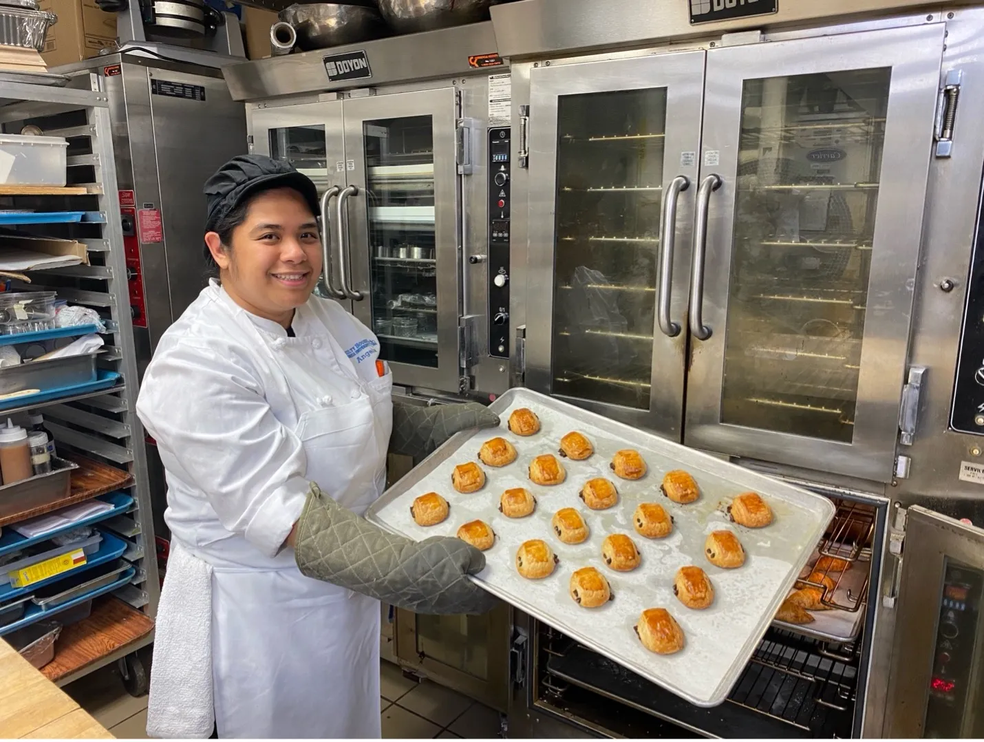 Rounds Cook Angela Acorita removes freshly baked pain au chocolat from the oven.